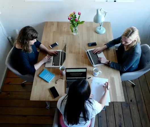 Three people working on laptops and notes around a shared table