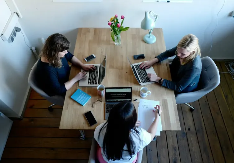 Three people working on laptops and notes around a shared table
