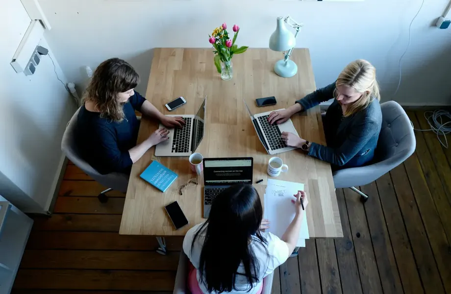 Three people working on laptops and notes around a shared table