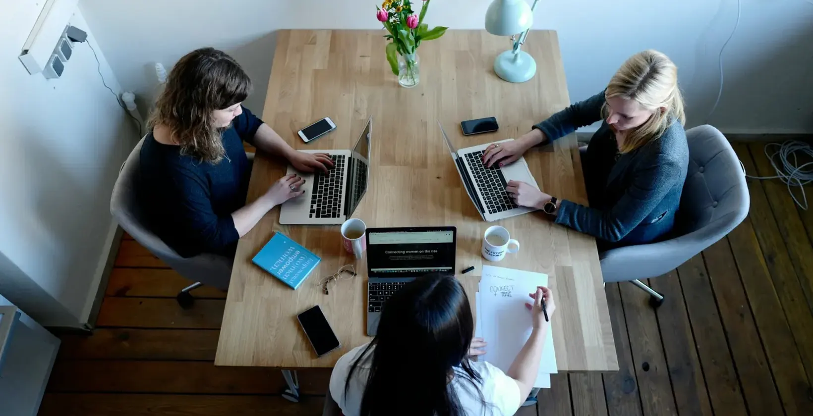 Three people working on laptops and notes around a shared table
