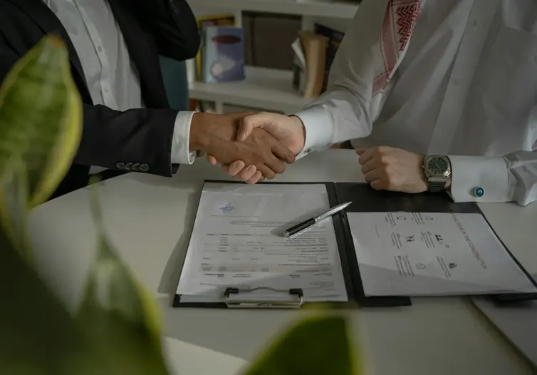 Two people shaking hands across a desk with signed documents