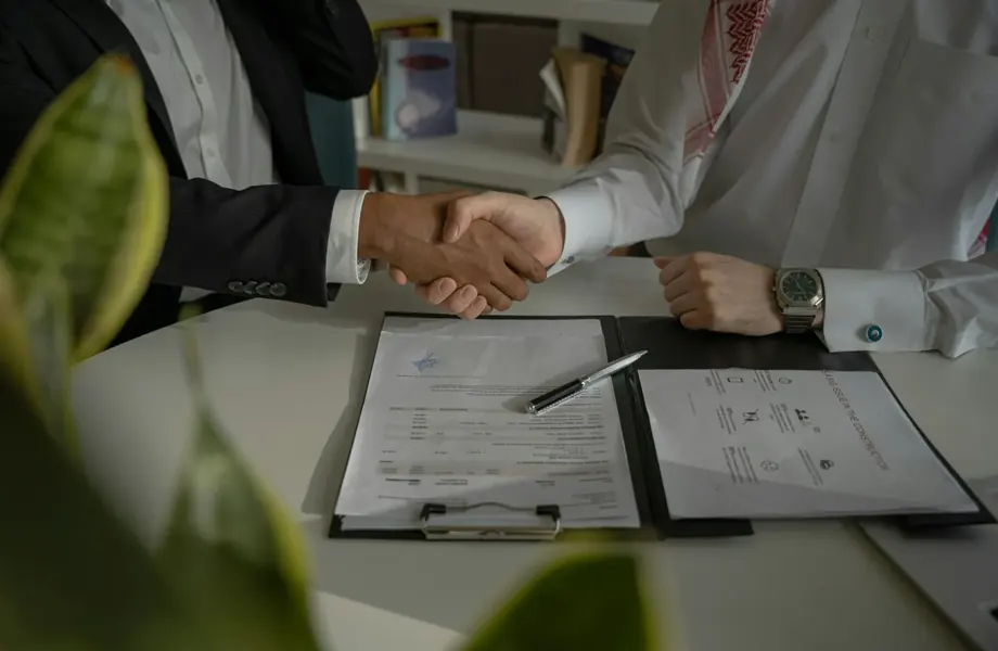 Two people shaking hands across a desk with signed documents