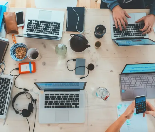 Several people working on laptops and phones at a shared desk, seen from above