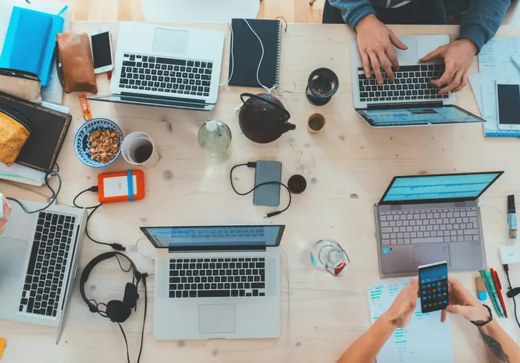 Several people working on laptops and phones at a shared desk, seen from above