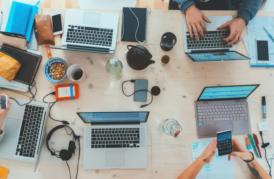 Several people working on laptops and phones at a shared desk, seen from above