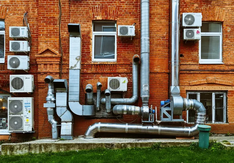 Air conditioning units and ductwork on the outside wall of a brick building